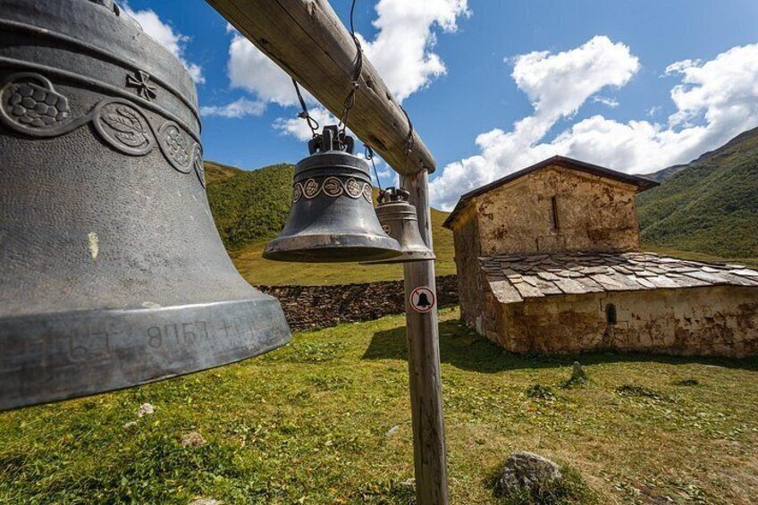 Una campana grande, una campana más pequeña y un edificio rústico en un paisaje montañoso. 4