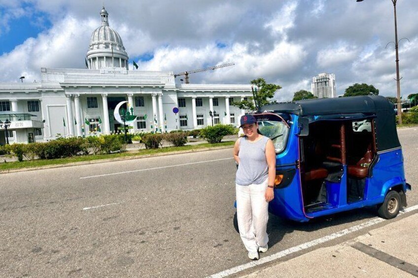 A person standing next to a blue auto-rickshaw on a street with a large white building with a dome and crescent moon decorations in the background. 3