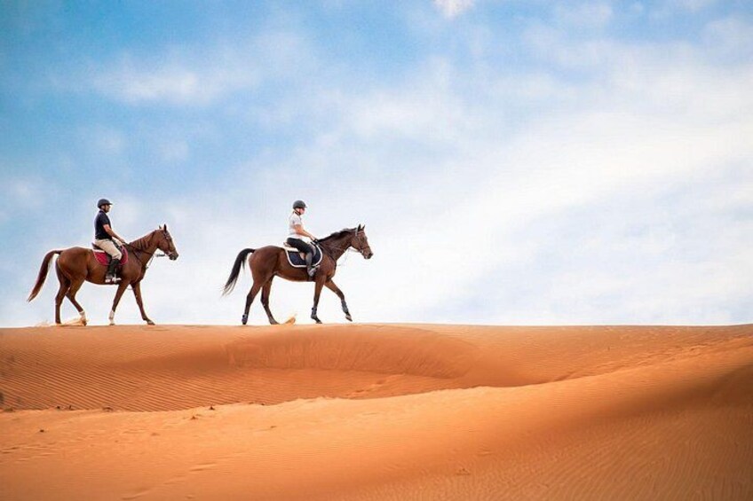 Two people riding horses across a desert landscape with sand dunes. 2