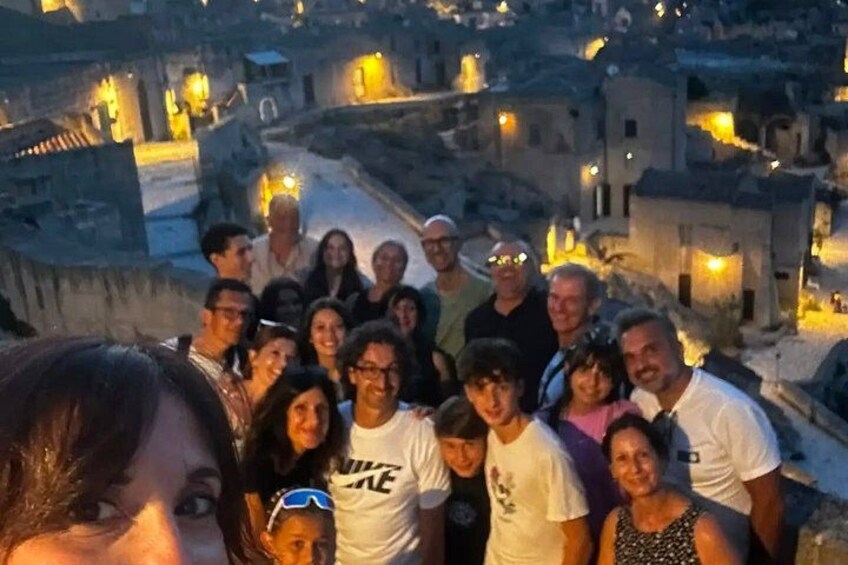 A group of people standing on a rooftop overlooking a town at dusk. 2