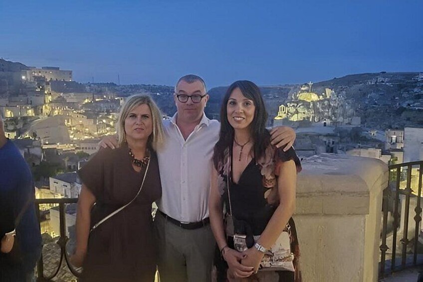 Three people standing on a balcony with a cityscape in the background. 5