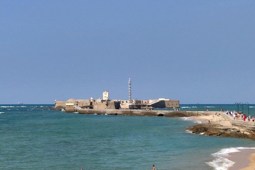 Una fortificación costera con un faro, playa y gente caminando por la orilla. 5