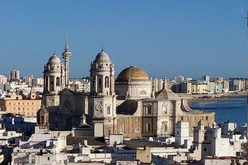 Un paisaje urbano costero con arquitectura histórica destacada, incluyendo una iglesia grande con dos cúpulas y una cúpula central, sobre un fondo de edificios urbanos y un cielo despejado. 2