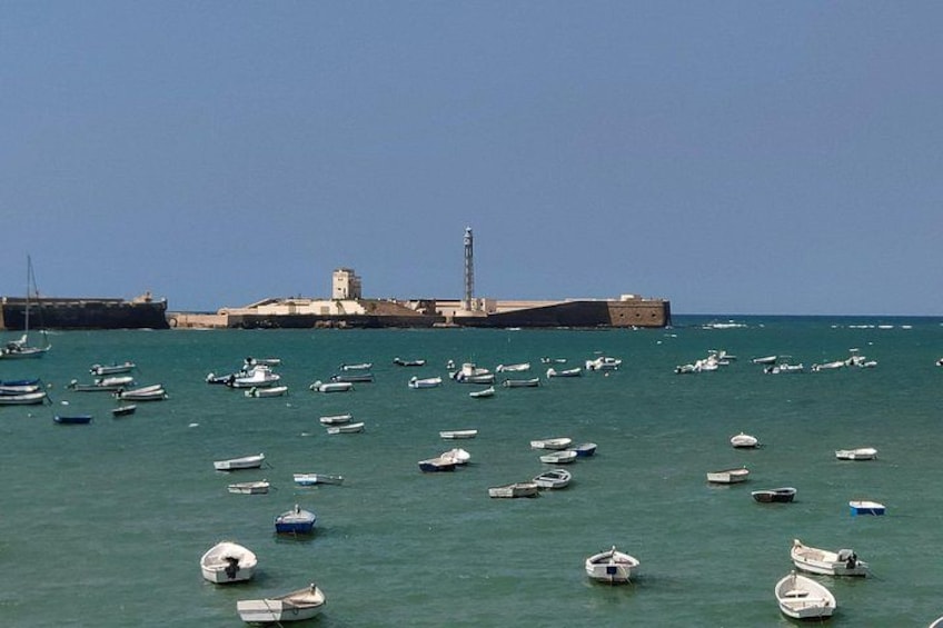 Un puerto con numerosos barcos, un faro y una estructura fortificada al fondo. 4