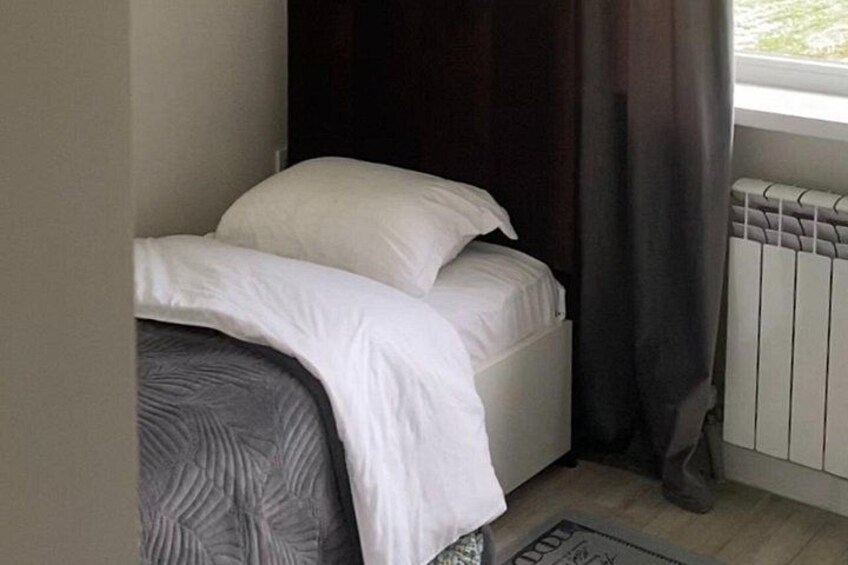 A bed with white bedding, a dark curtain, and a radiator. 4