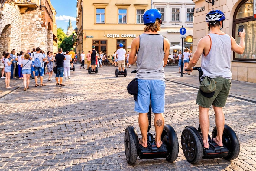 Kaksi ihmistä segway-lautoilla, mukulakivikatu ja rakennus, jonka kyltissä lukee: ”Costa Coffee”. 3