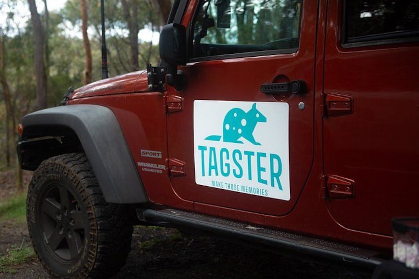 Un vehículo todoterreno rojo con el logotipo 'TAGSTER' y el lema 'MAKE THOSE MEMORIES' en su lateral. 2