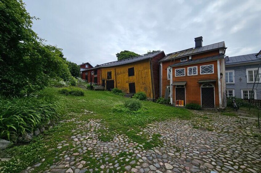 A cobblestone pathway leading to a row of wooden houses with a grassy area and trees on the left. 3