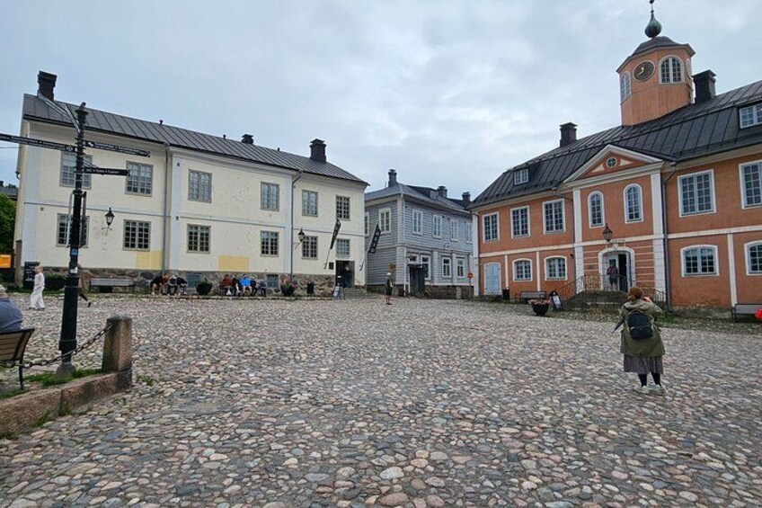 A cobblestone street with historic buildings, a person walking, and a clock tower. 2
