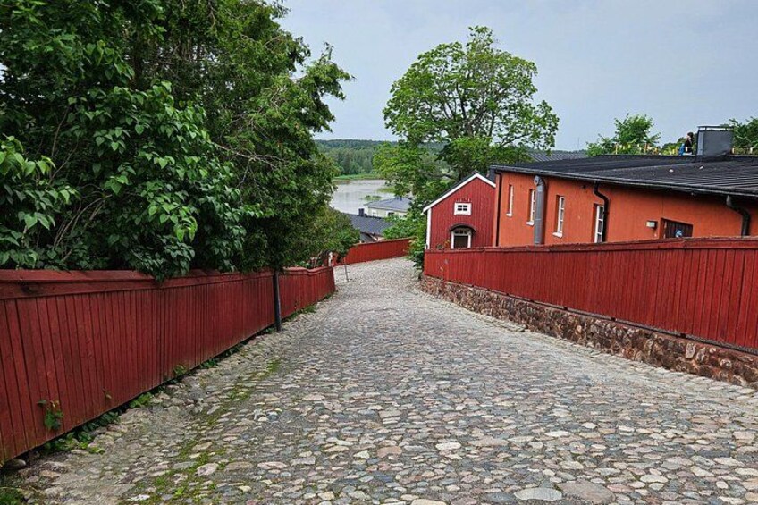 A cobblestone path leading to a red building with a black roof, surrounded by a red fence and greenery. 3