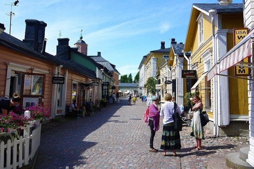 En kullerstensgata kantad av gula och vita byggnader, ett vitt trästaket och människor som promenerar. 3