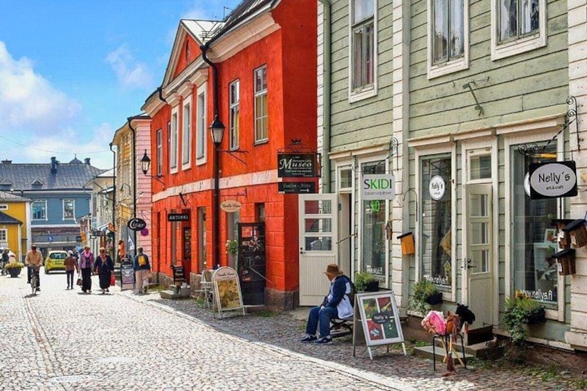 A cobblestone street with historic buildings, a red building with a sign 'Mats' and a green building with a sign 'SKIDI'. 1