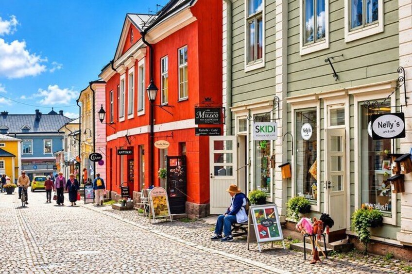 En kullerstensgata kantad av färgglada byggnader, inklusive en röd byggnad med en skylt som visar texten ”MESCO” och en grön byggnad med en skylt som visar texten ”Nelly’s”. 1