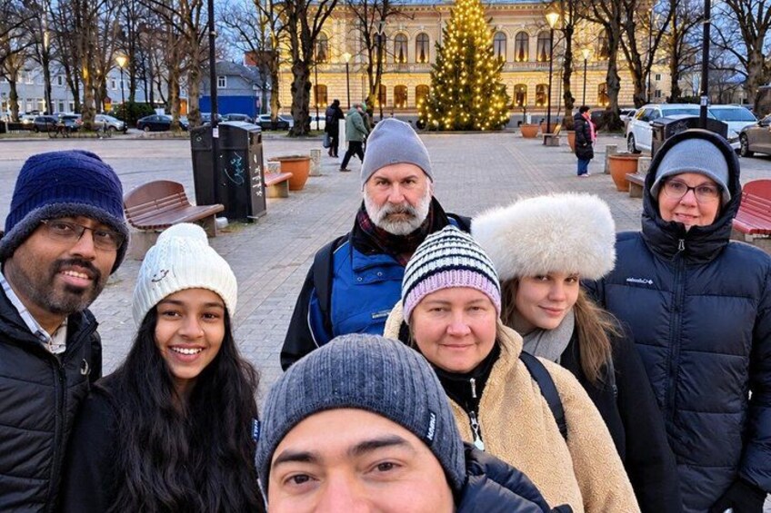 En grupp människor utomhus, med ett julgran och en byggnad i bakgrunden. 2