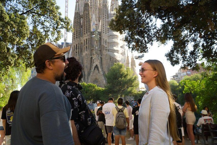 A group of people standing outdoors, a large building in the background, and trees around them. 3