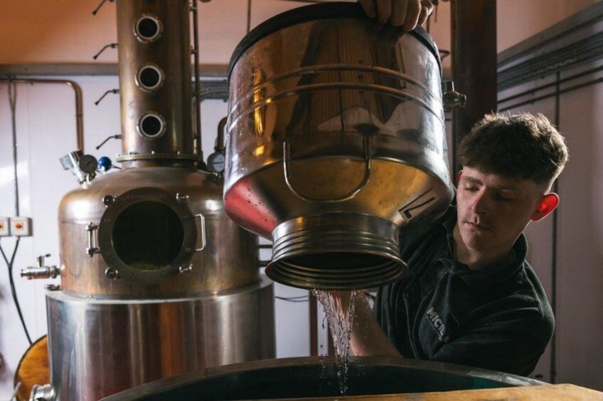 A person pouring liquid from a large metal container into a tank. 5