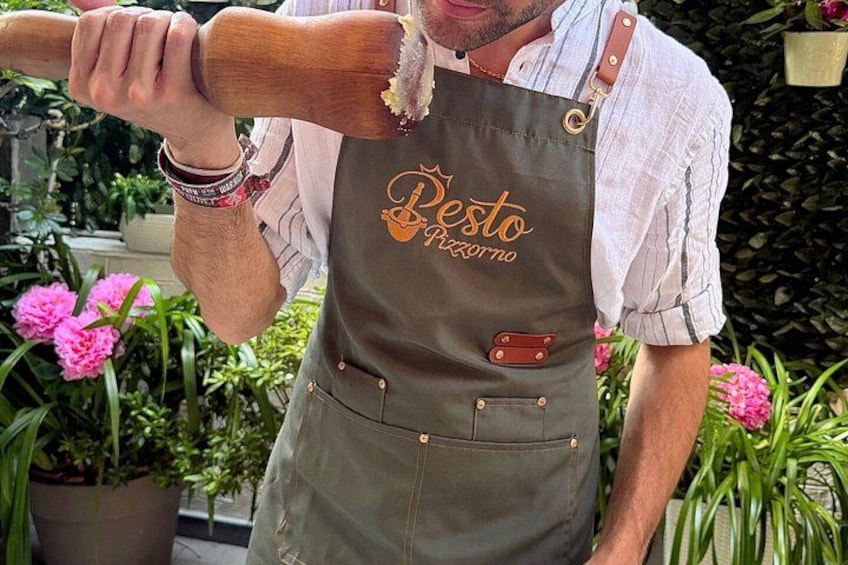 Une personne portant un tablier « Pesto Pizzeria » et tenant un rouleau à pâtisserie en bois. 4