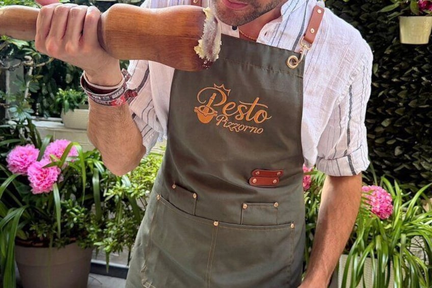 Een persoon in een 'Pesto Pizzeria' schort, met een deegroller in de hand. 5