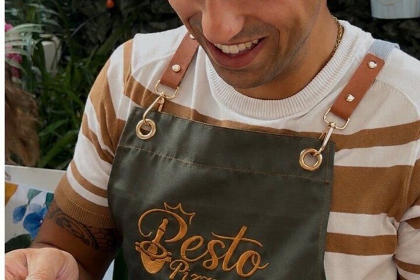 Een persoon draagt een geruit shirt en een donkere schort, waarop 'Besto Pasta' geborduurd staat. 3