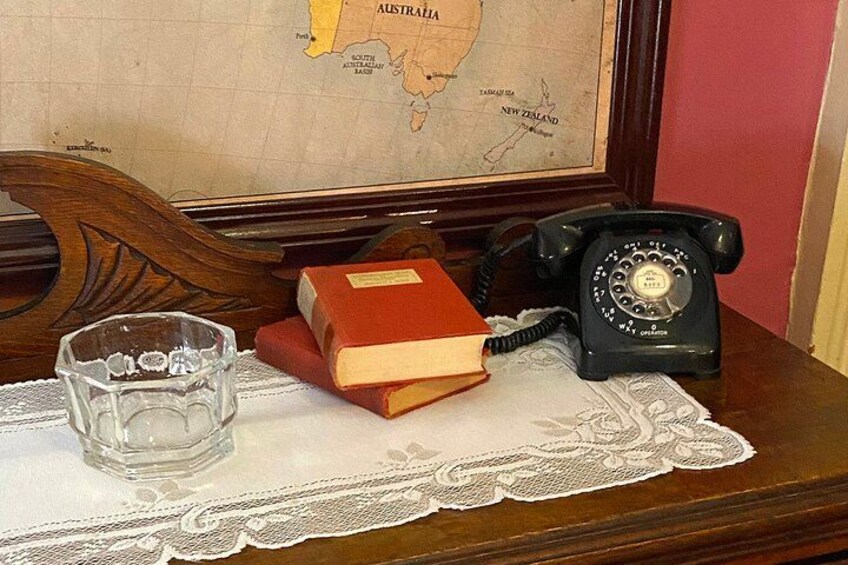A wooden table with a lace tablecloth, a glass ashtray, a red book, and a black rotary phone. 3