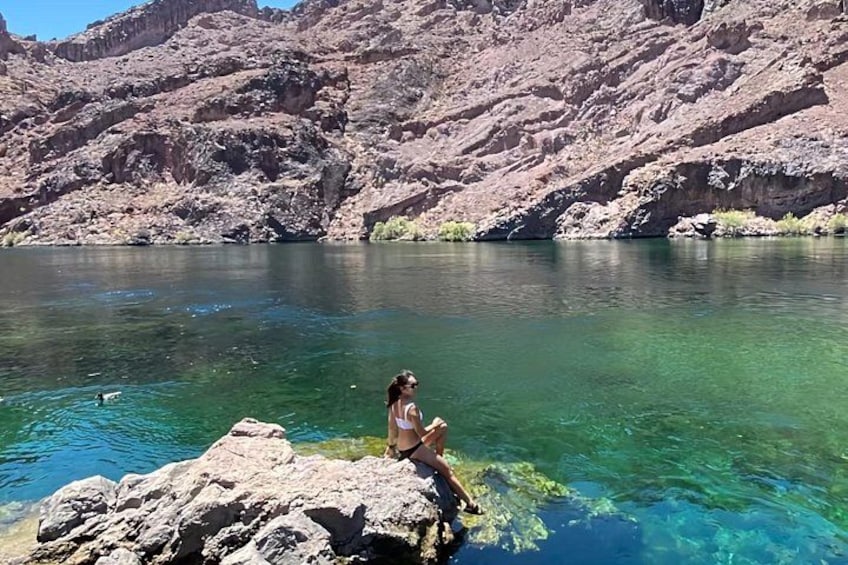 Une personne assise sur un rocher, au bord d’un lac aux eaux d’un bleu limpide, avec des montagnes en arrière-plan. 3