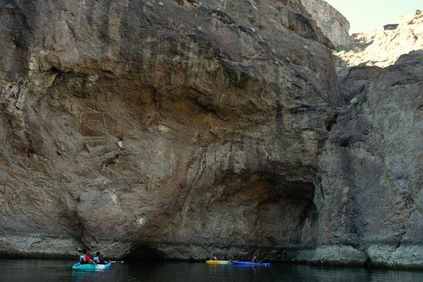 Une falaise rocheuse avec une entrée de grotte et des kayaks près de l’eau. 4