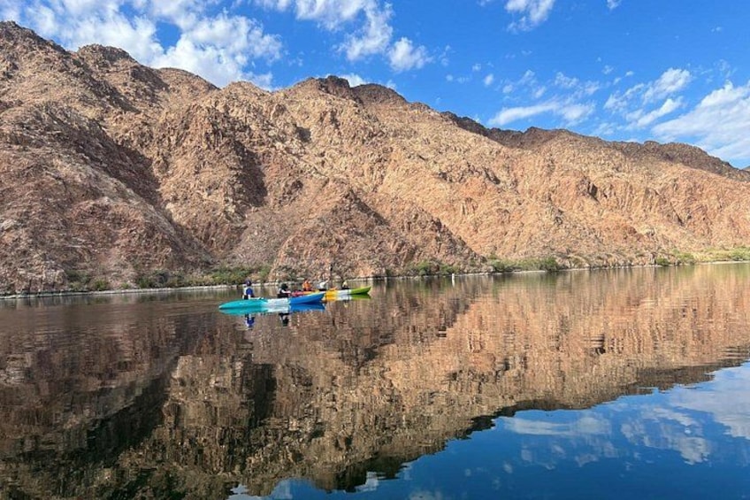 Un lac paisible où se reflètent les montagnes rocheuses environnantes, un groupe de kayaks et un ciel bleu clair. 5