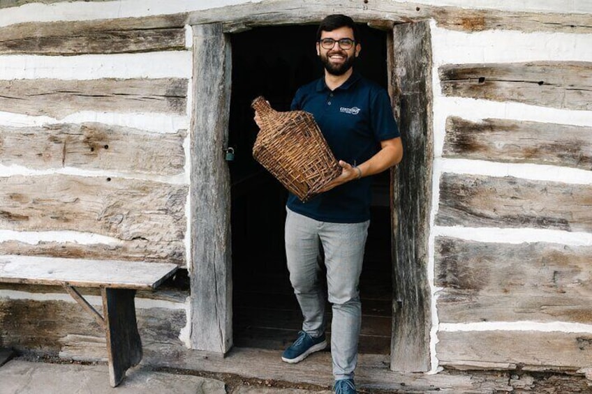 A person standing at the entrance of a log cabin holding a woven basket. 2