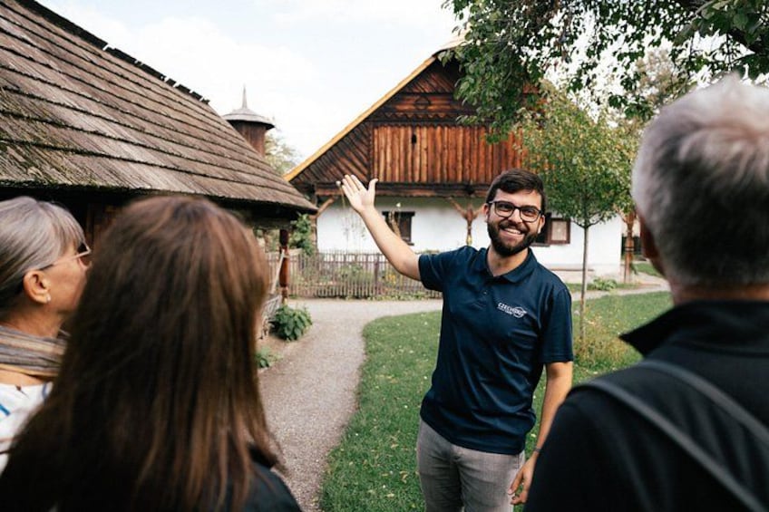 A person in a blue shirt standing in a rural setting with wooden buildings and a pathway. 1