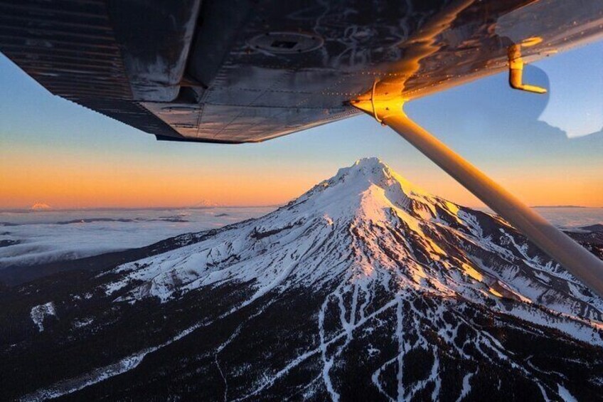 A snow-covered mountain at sunset with an airplane wing in the foreground. 2