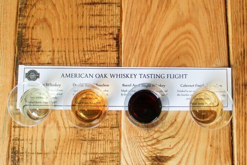 Une table en bois sur laquelle sont disposés plusieurs petits verres de whisky américain vieilli en fût de chêne, ainsi qu’une bouteille dont l’étiquette indique le prix et trois verres de whisky. 2