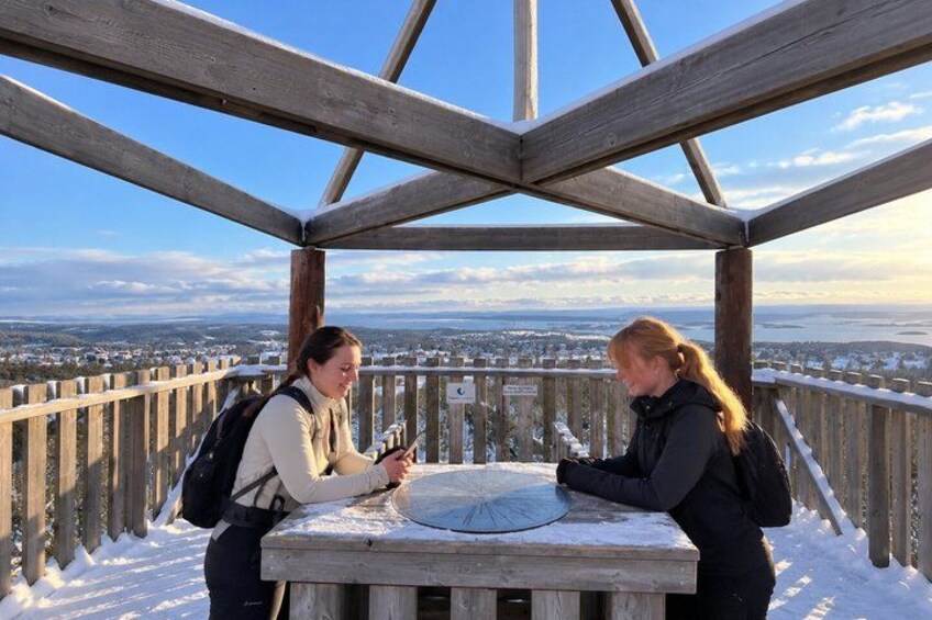 Two people at a wooden observation deck with a snowy landscape in the background. 1