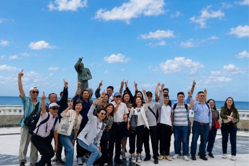 A group of people posing in front of a statue on a sunny day. 4