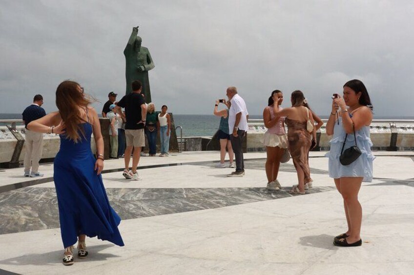 A group of people at a waterfront promenade with a statue in the background. 3