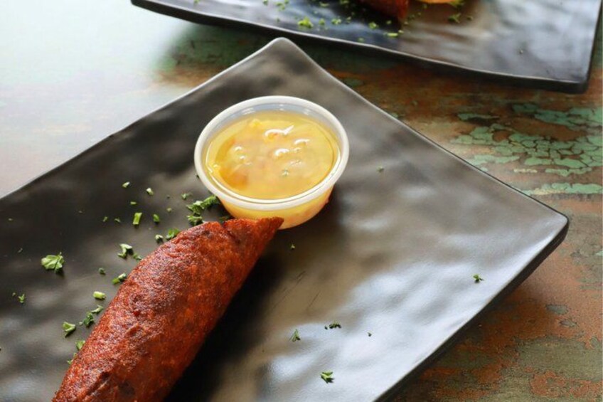 A grilled meat on a dark plate with a small bowl of sauce and some herbs. 2