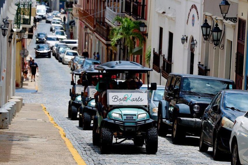 A cobblestone street lined with parked cars and a golf cart with a sign. 5