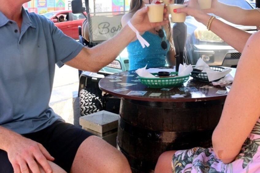 A person pouring a drink into a cup at a table with a green basket and a bottle. 3