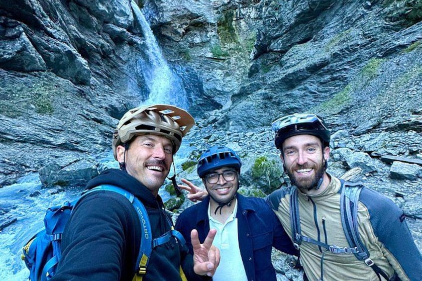 Drei Personen mit Helmen und Rucksäcken vor einem Wasserfall. 5