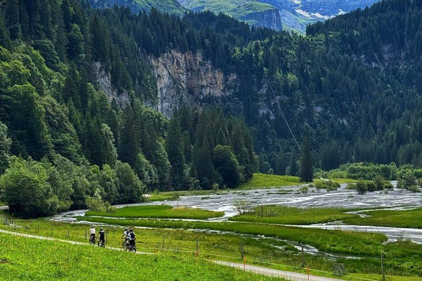 Ein Fluss mit Radfahrern, umgeben von üppiger Vegetation und Bergen. 2