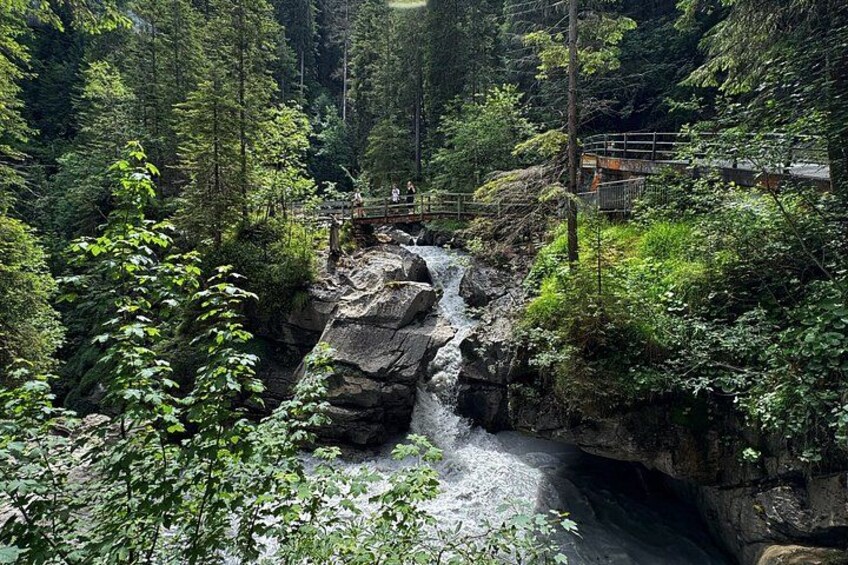 Ein Wasserfall in bewaldeter Landschaft mit einer Holzbrücke. 4