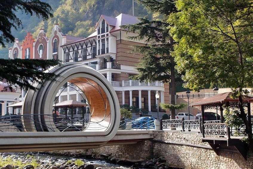 A modern bridge with a circular design, a stone pathway, and traditional buildings in the background. 3