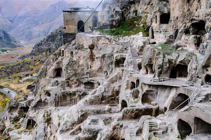 A rocky cliff with ancient cave dwellings and a staircase leading up. 5