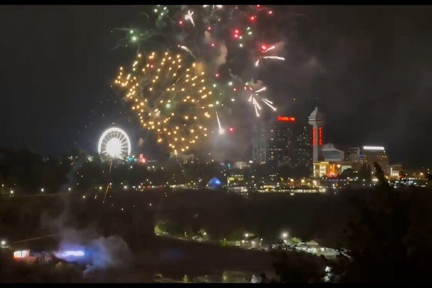 Stadtbild mit Feuerwerk, Riesenrad und hohem Gebäude mit rotem Schild. 2
