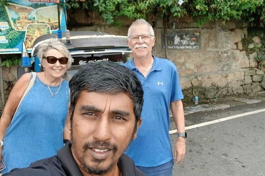 Three people standing in front of a vehicle and a stone wall with greenery. 2