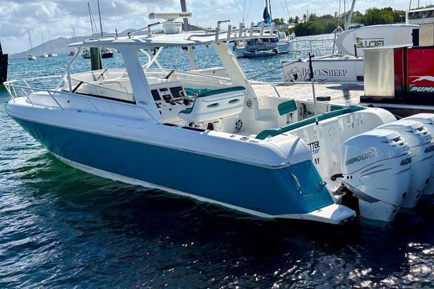 A blue and white motorboat docked at a marina with other boats in the background. 1