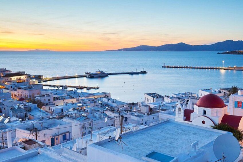 A coastal town at sunset with buildings, a pier, and a calm sea. 1