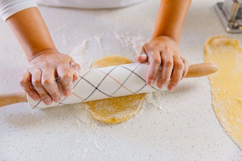 Hands rolling dough with a patterned rolling pin on a floured surface. 2