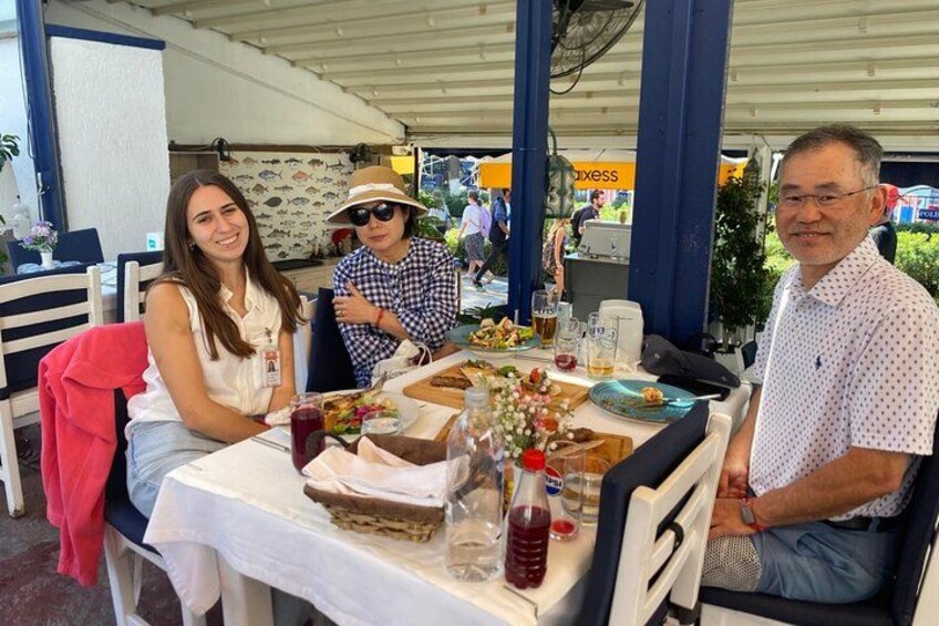 En gruppe mennesker spiser på en udendørs restaurant ved et bord med mad og drikke. 4