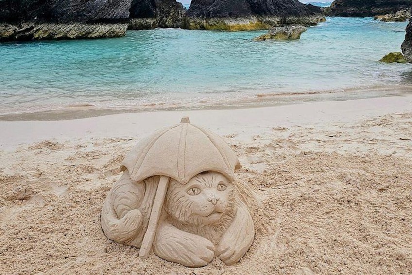 Eine Sandskulptur einer Katze mit einem Regenschirm am Strand. 3