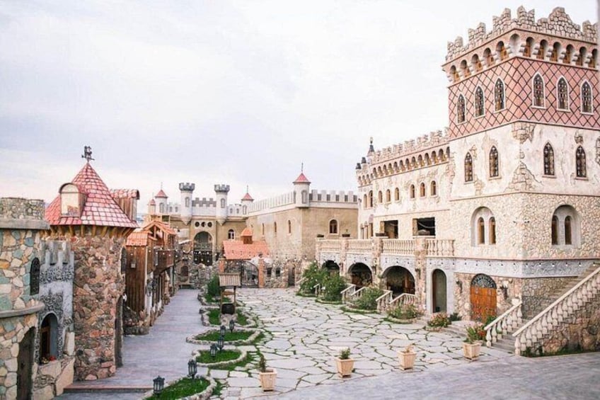 Un patio de castillo con senderos de piedra, arcos y una torre central. 3